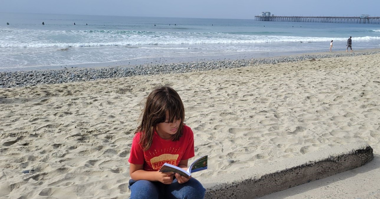 Girl reading chapter book on the beach
